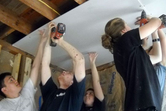 Students hold power tools while drilling a piece of material into place