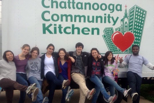 Students kick their legs out in a pose while leaning against a Chattanooga Community Kitchen truck