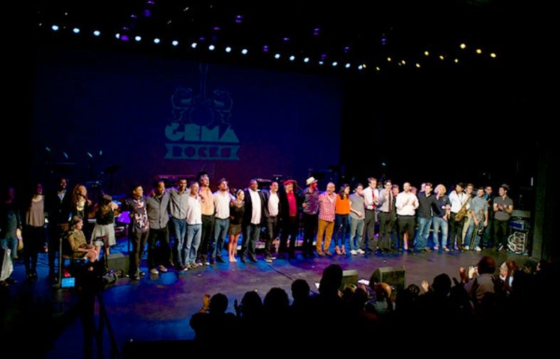 Dozens of people in the GEMA Rocks Company stand on stage