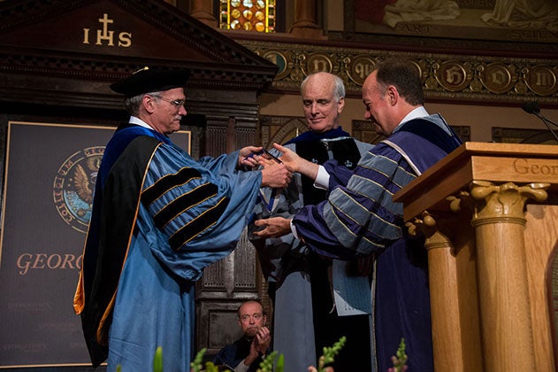 Robert Groves and President DeGioia award James Collins with one of three Presidential Fellow medals onstage in Gaston Hall. 