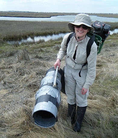 Amy Battocletti stands in a salt marsh and holds a piece of equipment.