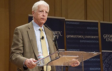 Jonathan R. Cole, wearing a tan suit, speaks to an audience from a podium.