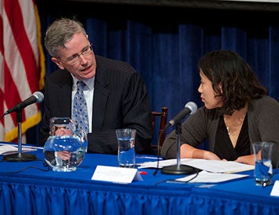 John Monahan, sitting behind a table, speaks as Susan Kim listens.