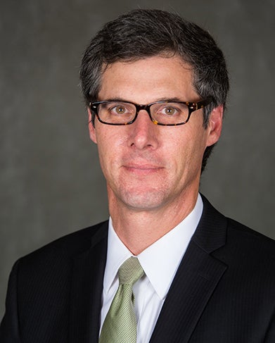 Keir Lieber, in glasses and a green tie, smiles for the camera in a headshot. 