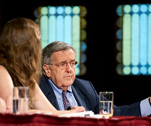 Mark Shields sits behind a table on Gaston Hall's stage.