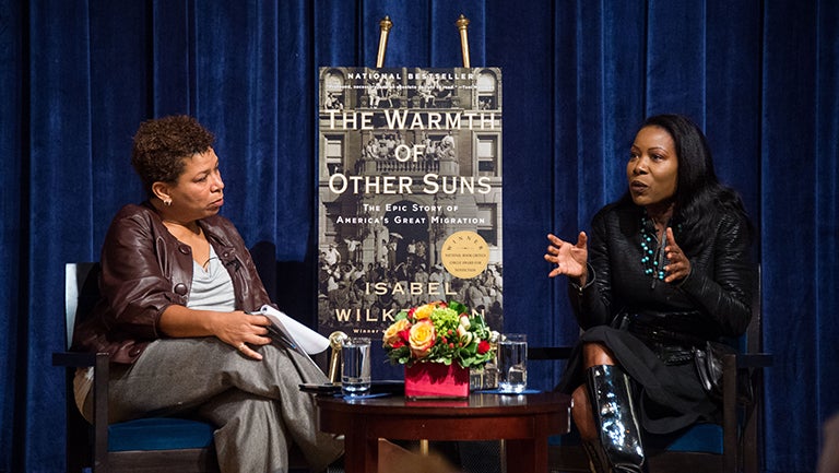 Michel Martin sits onstage with author Isabel Wilkerson, a large poster of Wilkerson's book titled "The Warmth of Other Suns" sits on a stand between them. 