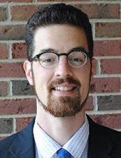 Alexander Thurston smiles for the camera against a brick wall.