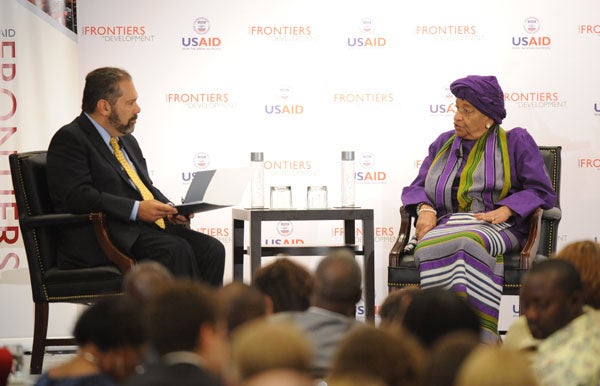 Ray Suarez talking with Ellen Sirleaf Johnson while seated at a table in front of a backdrop