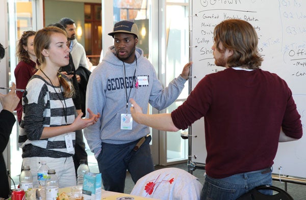 Three competitors discuss their idea while referencing things written on a whiteboard