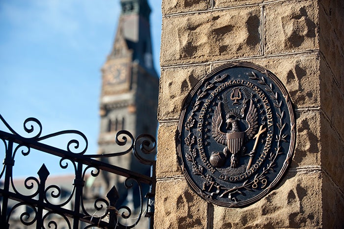 Picture of Georgetown University Seal at the Front Gates of Campus with Healy Hall in the background.