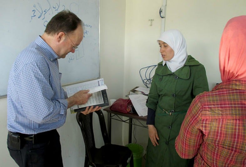 John J. DeGioia flips through a book while talking with two women in a classroom with a whiteboard