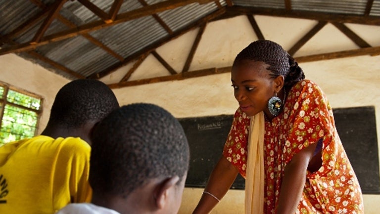 Teacher in Tanzania standing over two students seated