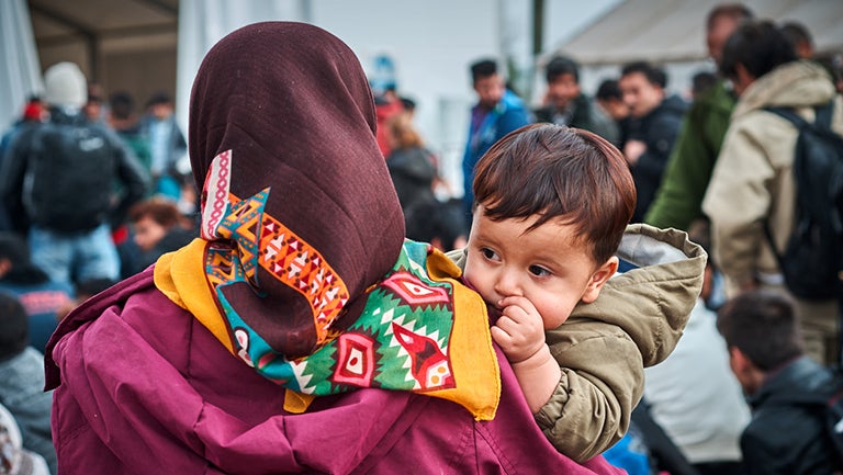 Syrian woman shown from back carrying baby in crowd