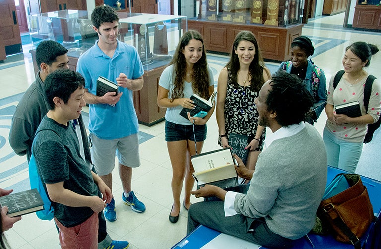 Students gather around author and alumnus Dinaw Mengestu with copies of his book