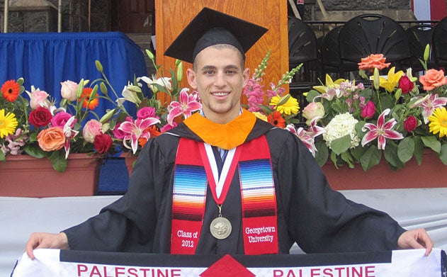 Raffoul Saadeh holds a Palestinian flag in front of flowers and a podium on stage