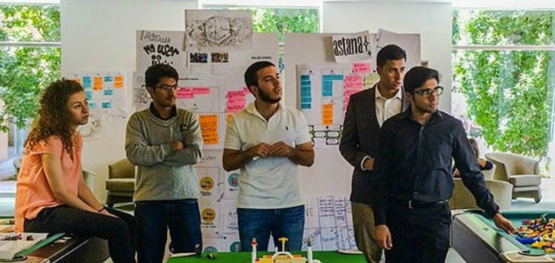 Fatima Sanz, Ahwaz Akhtar, Thanos Sardellis, Ahsan Malik, Haroon Yasin speak in front of posters with graphics