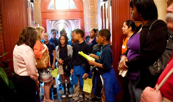 Sixth-graders stand in a hallway in Healy Hall listening to a woman speak