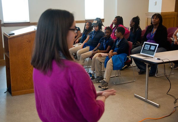 A woman presents to a group of sixth-graders seated in a classroom with a laptop on a table projecting material