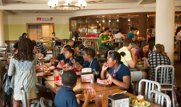 Students are seated at a table eating chicken fingers out of baskets with a pillar nearby