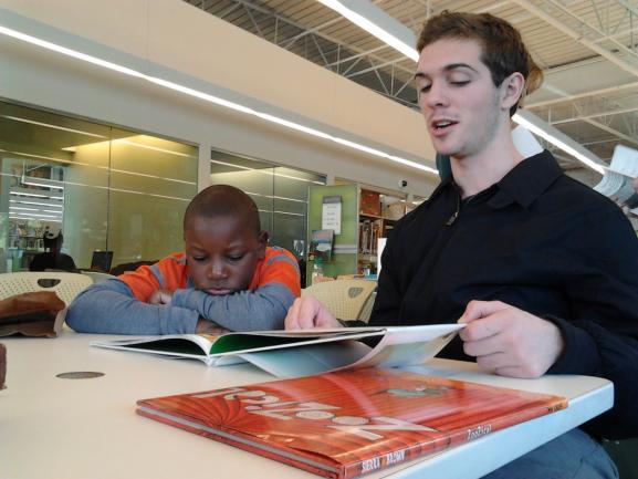 A student tutors a young student from a textbook