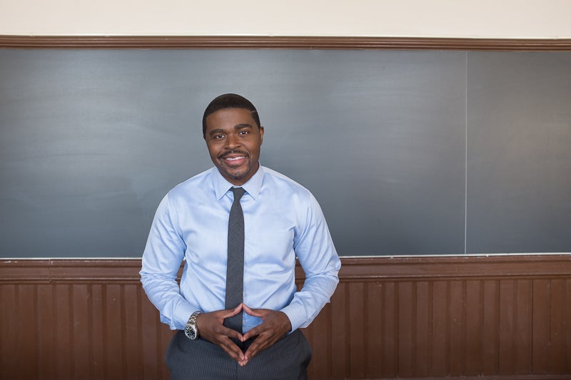 Professor Christopher King smiles for the camera in front of a chalkboard in a classroom.