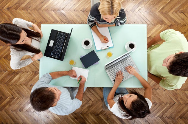 An overhead shot of a students working on a white table with laptops and notebooks. 